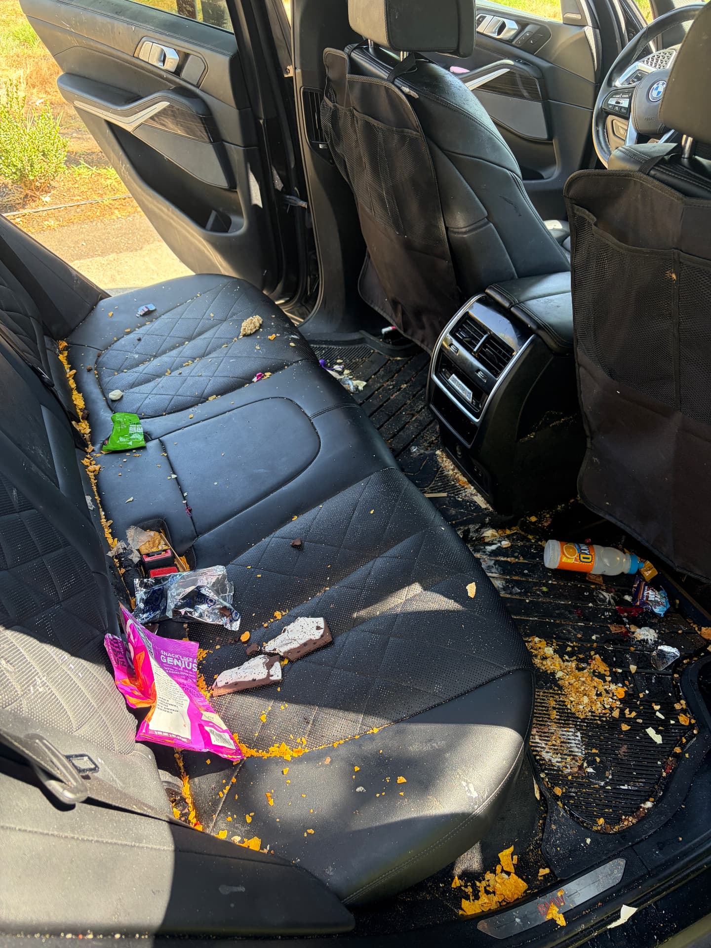 Dirty BMW back seat with crumbs, wrappers and debris before interior detailing